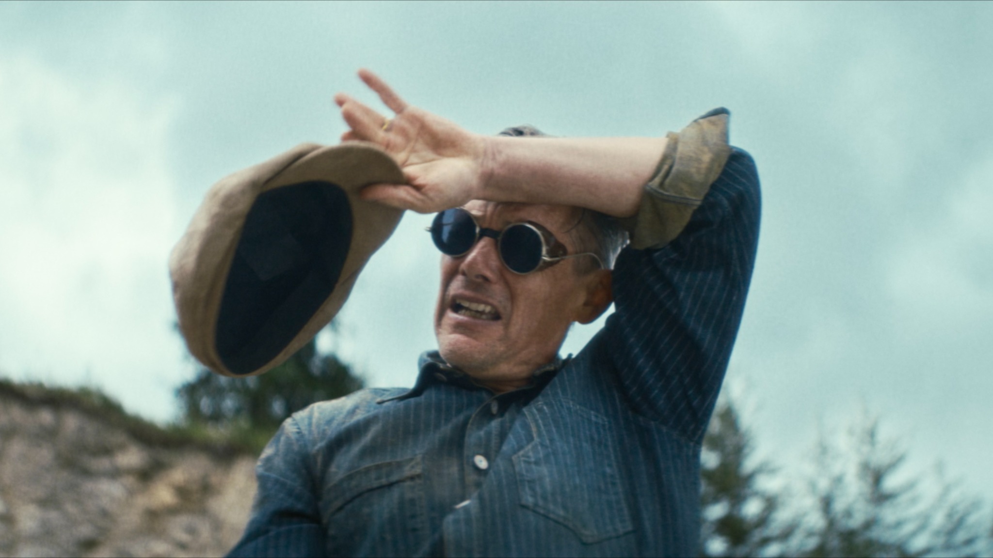 The Weight — a man in round sunglasses shielding himself with his hat